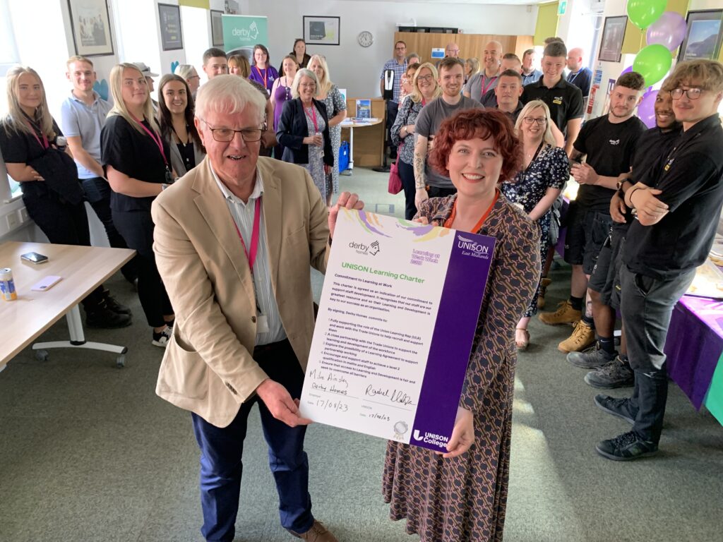 Mike Ainsley and Rachel Hodson hold the signed learning charter together with a group of workers in the background.